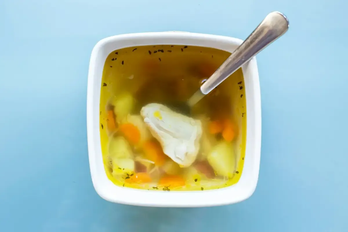 Sopa clara com pedaços de frango em tigela