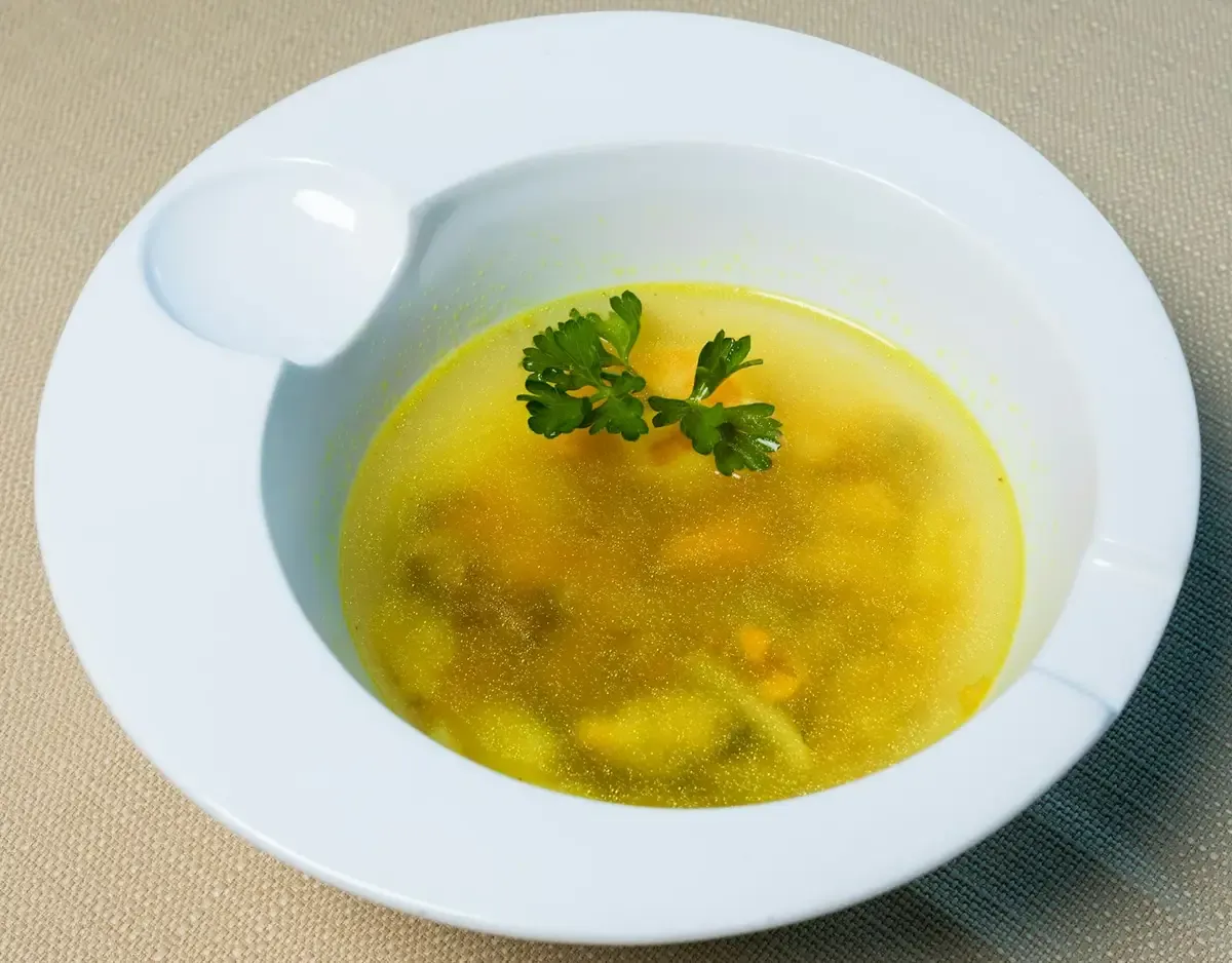 Caldo amarelo com ervas em prato fundo